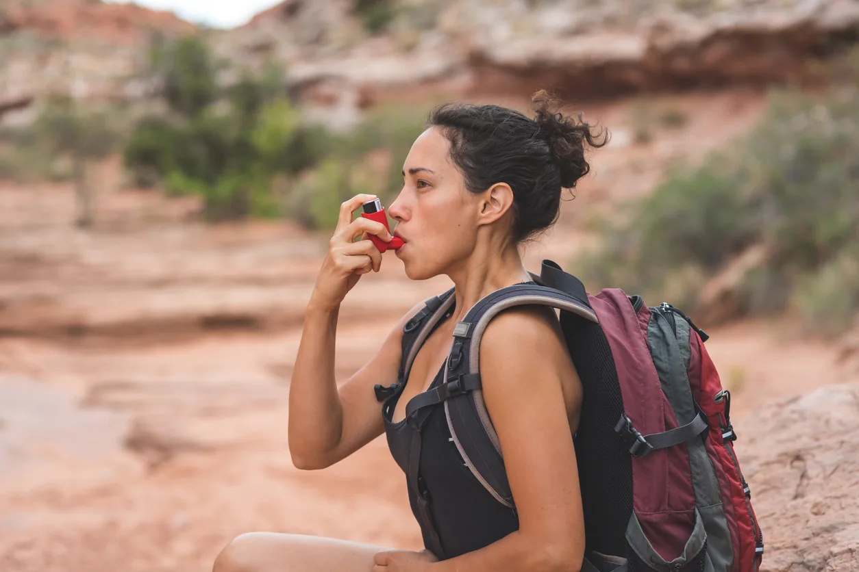 Woman using inhaler while hiking outdoors